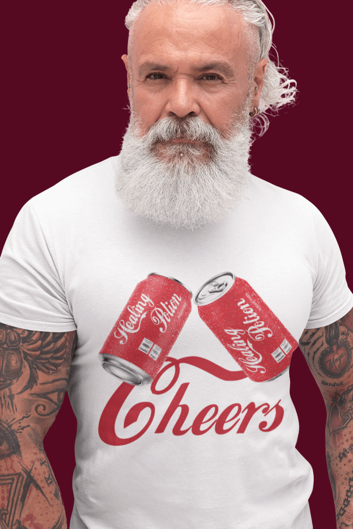 Grey-bearded man in white tee; two red 'Healing Potion' cans clink, 'Cheers' below; tattooed arms; burgundy background.